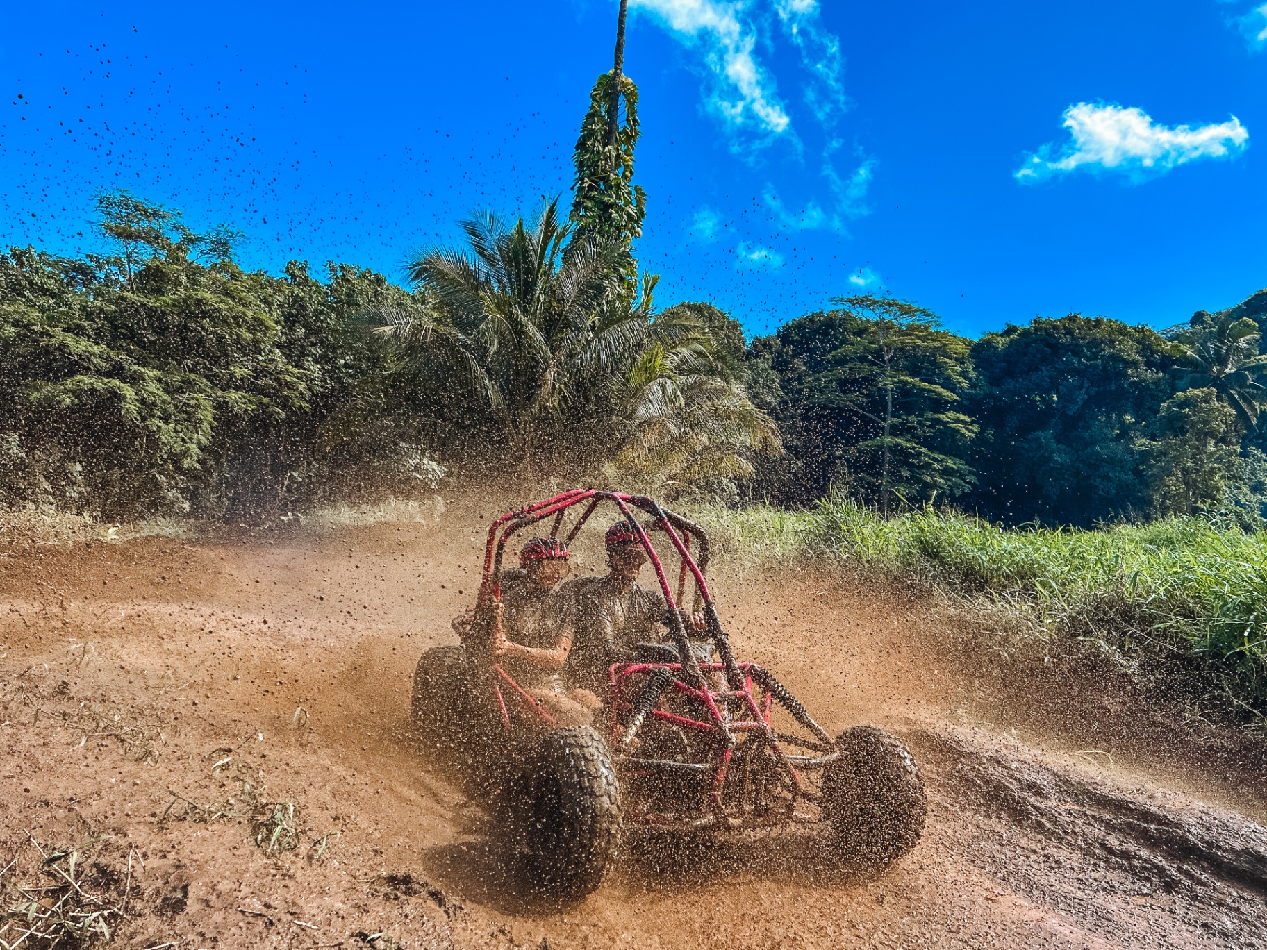 Two riders in a red buggy splashing through mud in Rarotonga