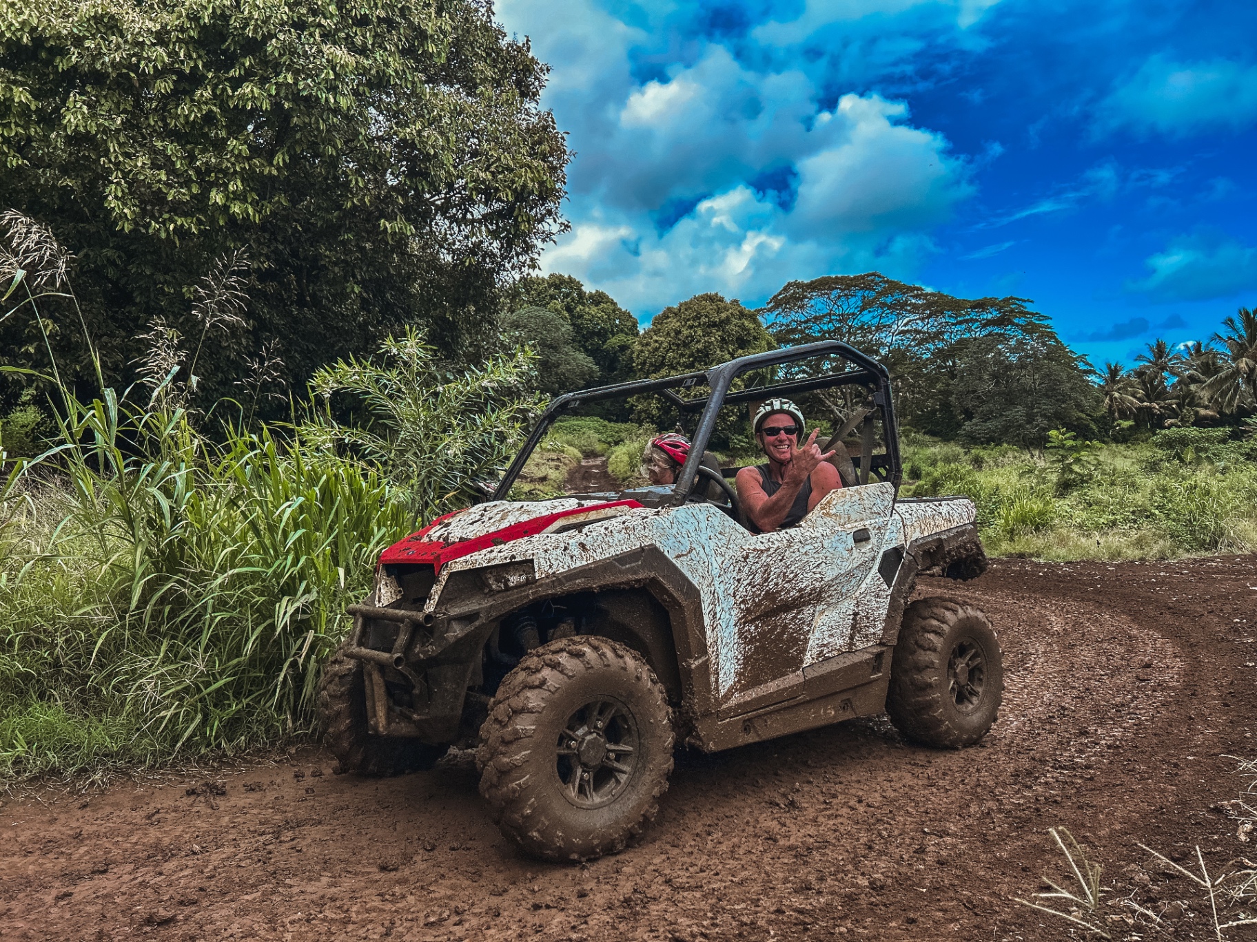 A mud-covered white buggy and smiling driver exploring Rarotonga's jungle