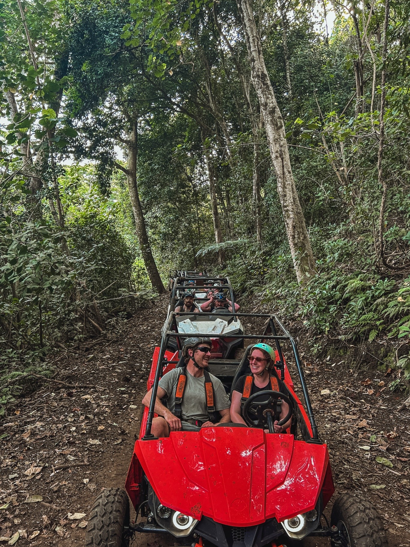 Helmeted guests smiling in their red buggy on a jungle trail